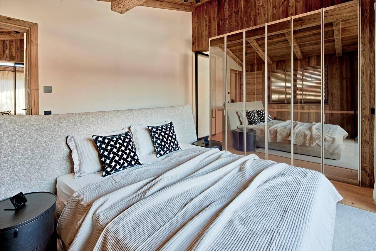 Modernes Schlafzimmer mit bequemen Bett, Holzbalkendecke und Spiegelschränken.