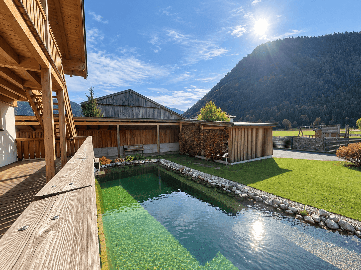 Sonniger Gartenbereich mit einem natürlichen Schwimmteich und Blick auf die bewaldeten Hügel.