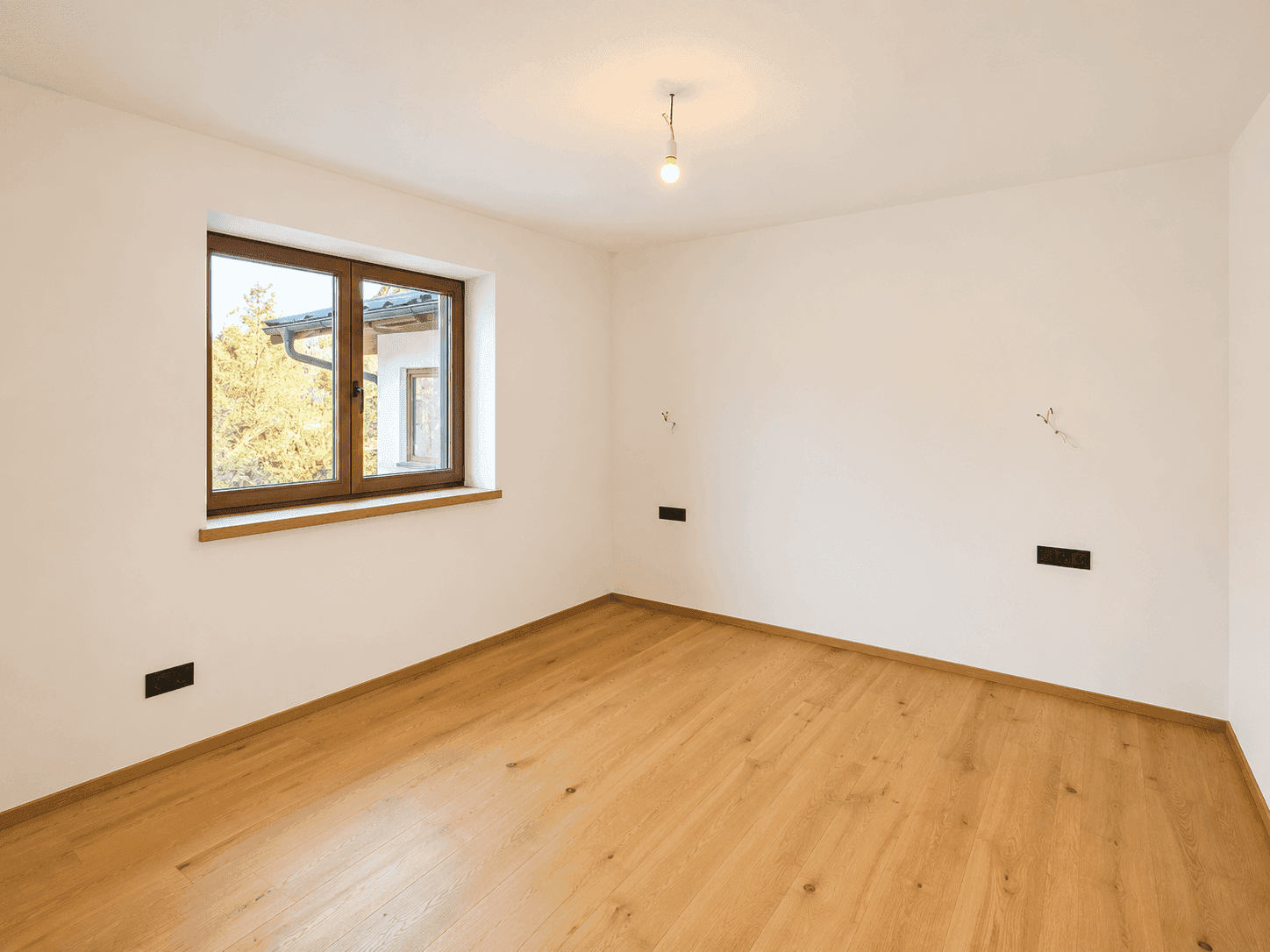 Helles, leeres Zimmer mit Holzboden und einem Fenster, bereit zur individuellen Gestaltung.