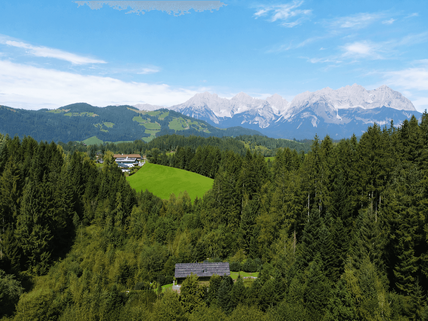 Beeindruckender Blick auf schneebedeckte Berggipfel, umgeben von dichten Wäldern und grünen Hügeln.