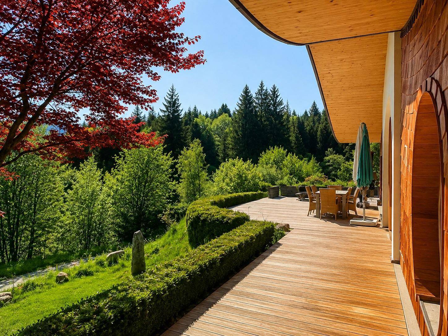 Geräumige Holzterrasse mit Essbereich und Hecke, umgeben von üppiger grüner Natur und Wald.