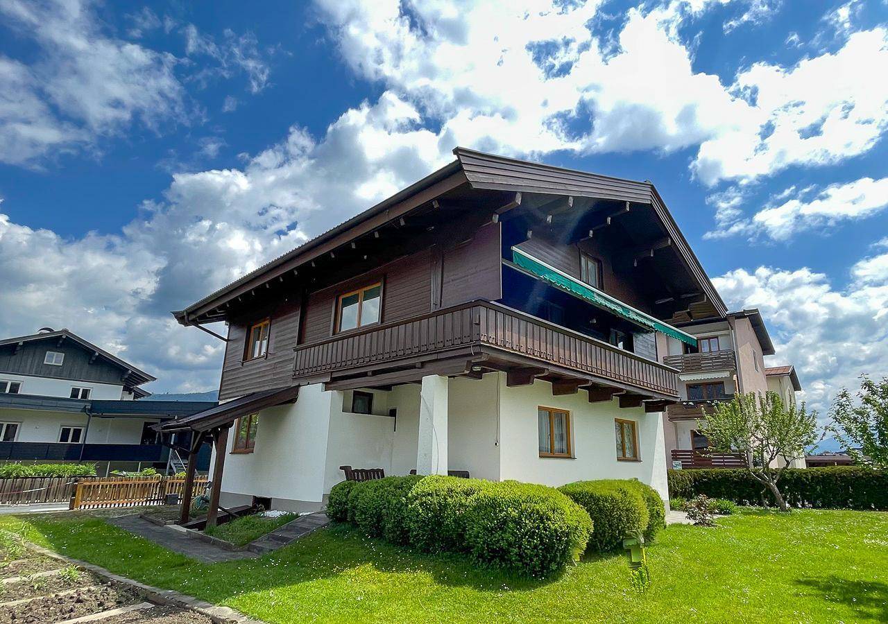 Seitenansicht des Hauses mit Balkon, grüner Markise und gepflegtem Rasen unter blauem Himmel.