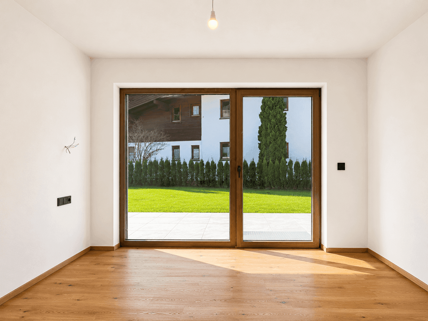 Leerer Raum mit Holzboden und großer Glasschiebetür zum Gartenbereich.