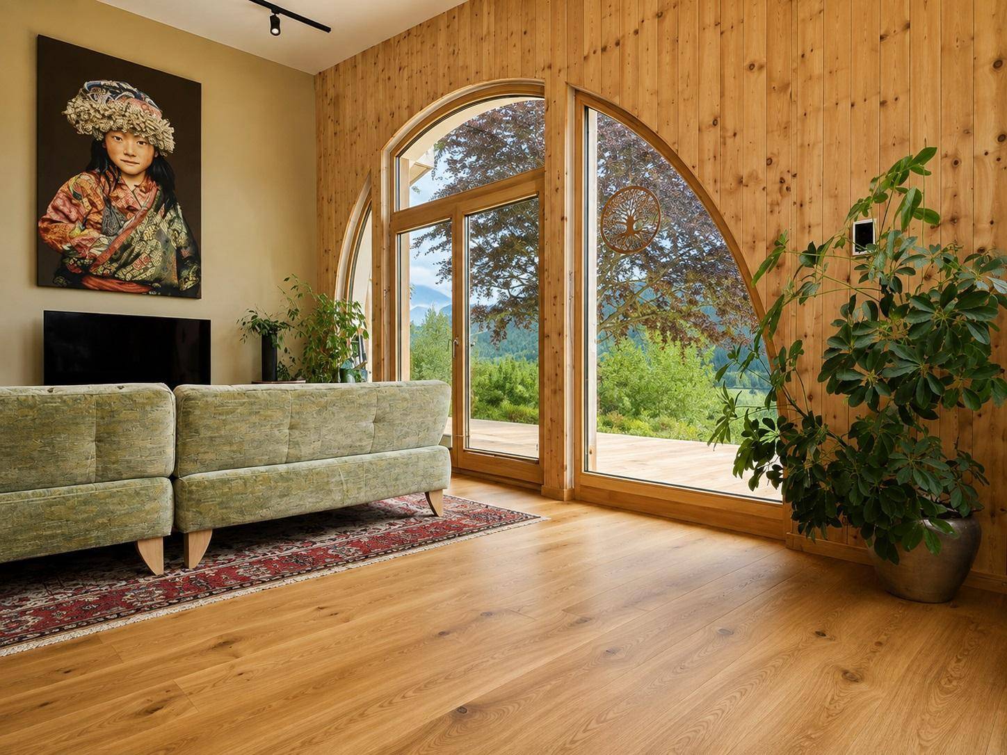 Gemütliches Wohnzimmer mit Holzwänden, bequemen Sofas und großen Bogenfenstern mit Blick ins Grüne.