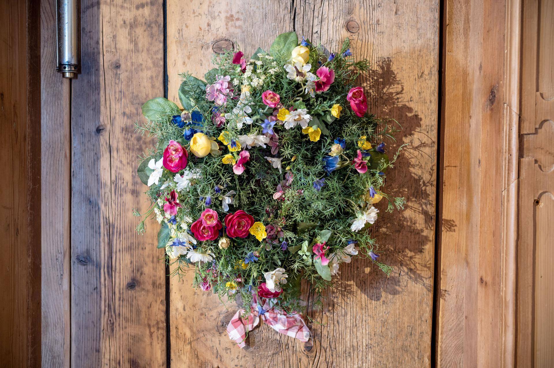 Nahaufnahme eines farbenfrohen Blumenkranzes an einer rustikalen Holztür.