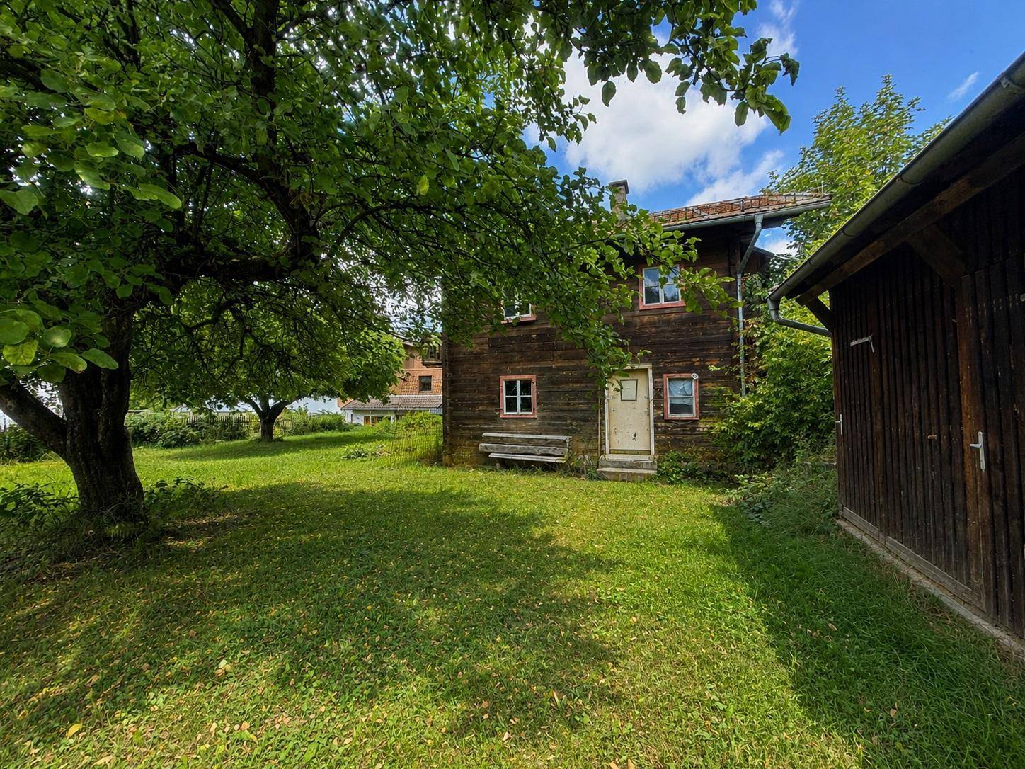 Rustikales Holzhaus mit weitläufigem Garten, einem kleinen Nebengebäude und viel Grünfläche.
