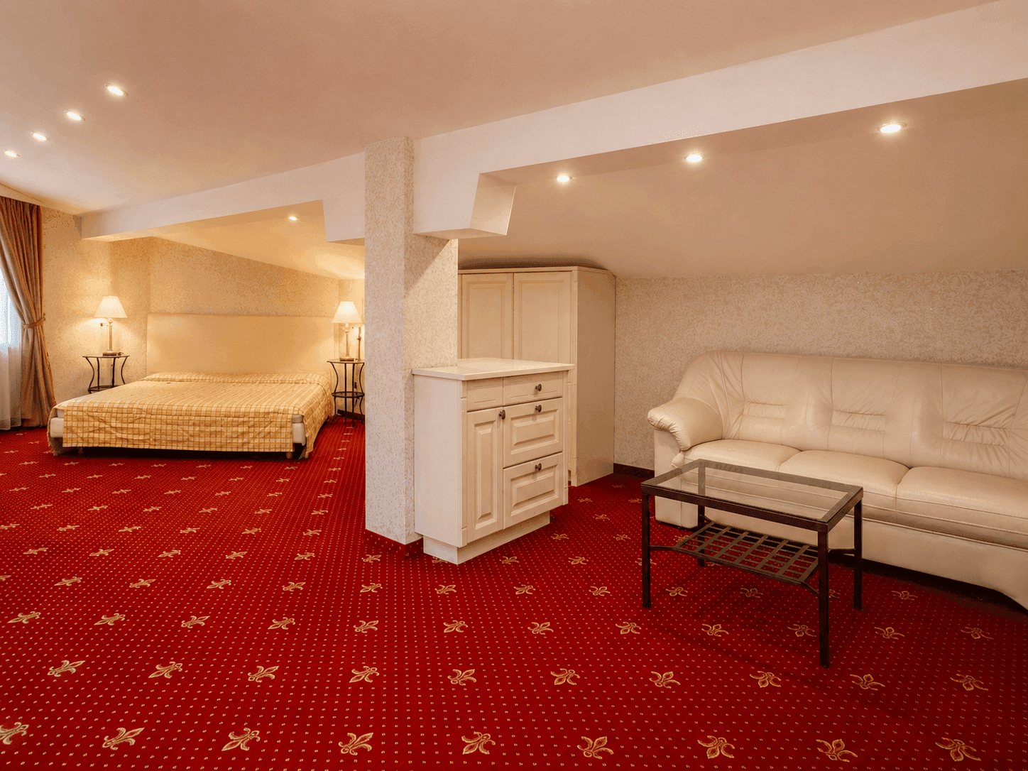 Geräumiges Schlafzimmer mit Doppelbett, Sofa und rotem Teppichboden im Dachgeschoss.
