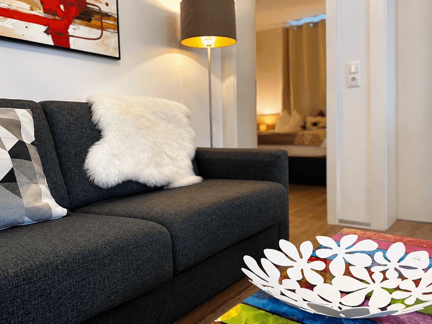 Gemütliches Wohnzimmer mit Sofa und Blick in ein angrenzendes Schlafzimmer, modern dekoriert.