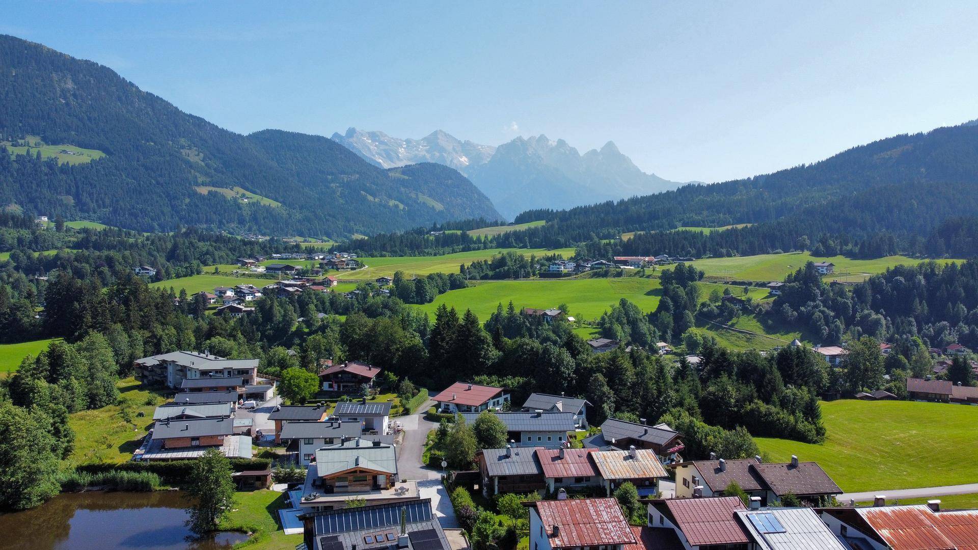 Malerische Landschaft mit Häusern, grünen Wiesen und Bergen im Hintergrund.