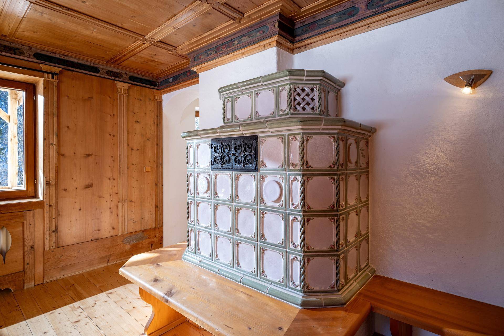 Detailansicht eines kunstvollen Kachelofens in einem traditionell eingerichteten Raum mit Holzboden.