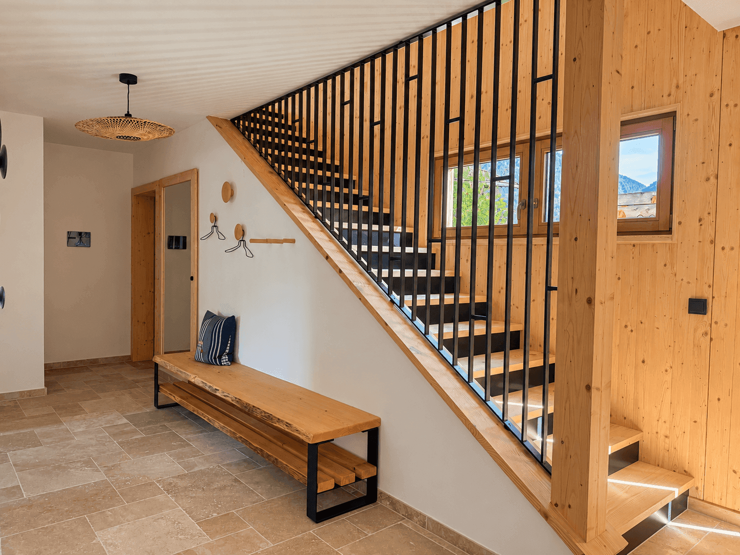 Heller Flur mit Holztreppe, modernem Geländer und Fliesenboden.