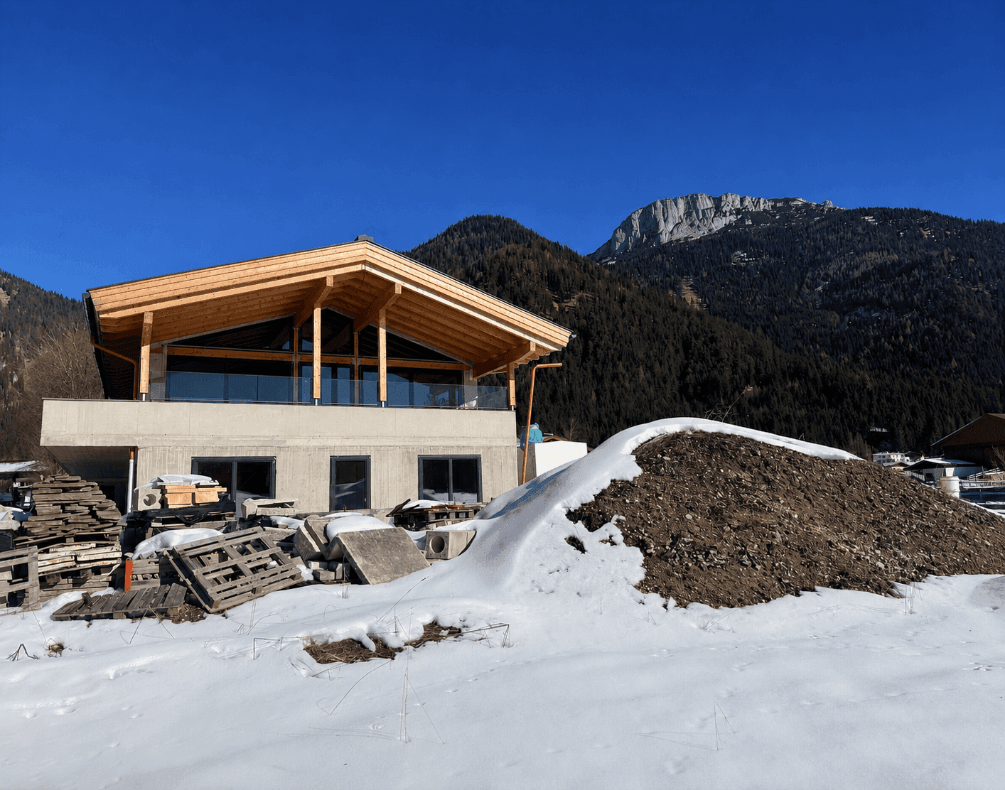 Neubau mit moderner Architektur und Holzdach in winterlicher Umgebung vor Bergkulisse.