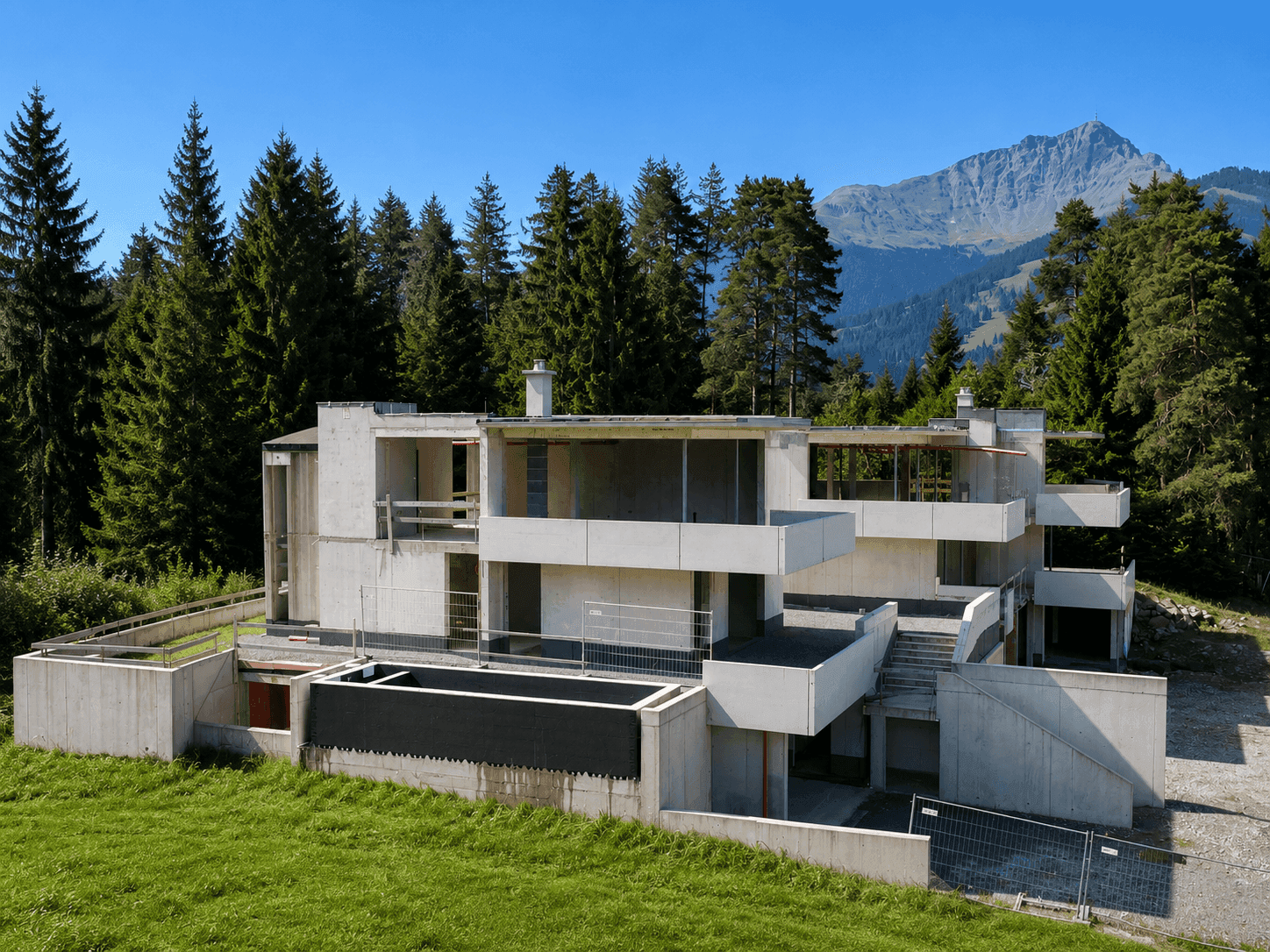 Rohbau einer modernen Wohnanlage mit Terrassen und Bergblick, umgeben von Wald und Wiesen.