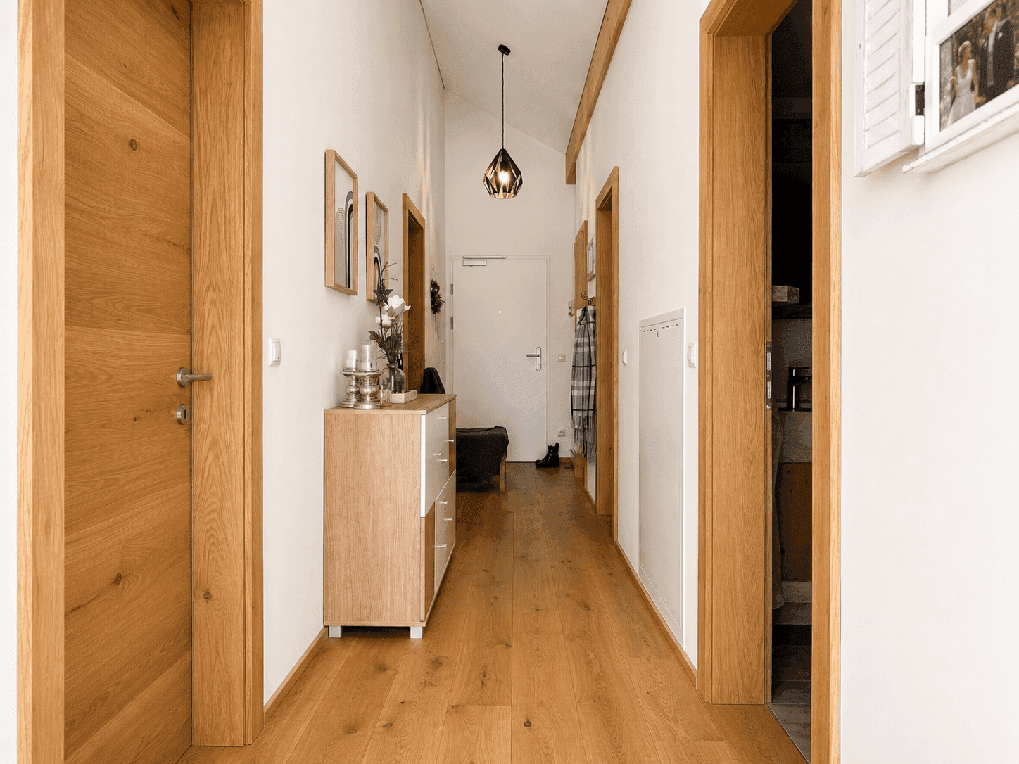 Heller Flur mit Holzboden, Holztüren und einer modernen Kommode, die den Eingangsbereich schmückt.