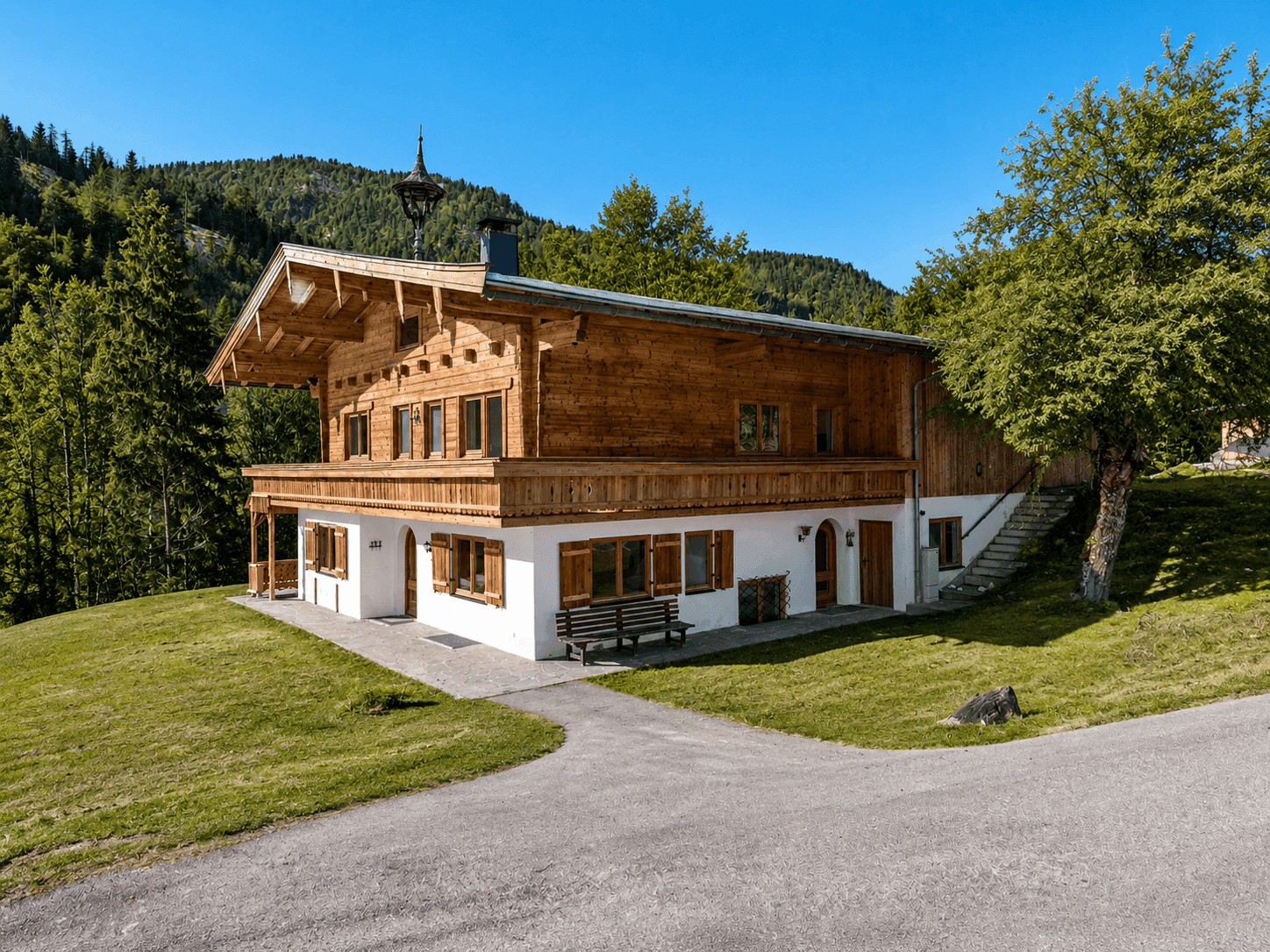 Charmantes Holzhaus mit traditionellen Elementen, umgeben von Bäumen und einer malerischen Berglandschaft.