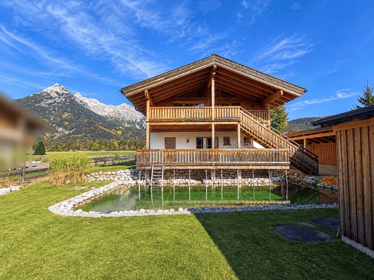 Traditionelles Holzhaus mit Bergblick und einem naturnahen Teich im gepflegten Garten.