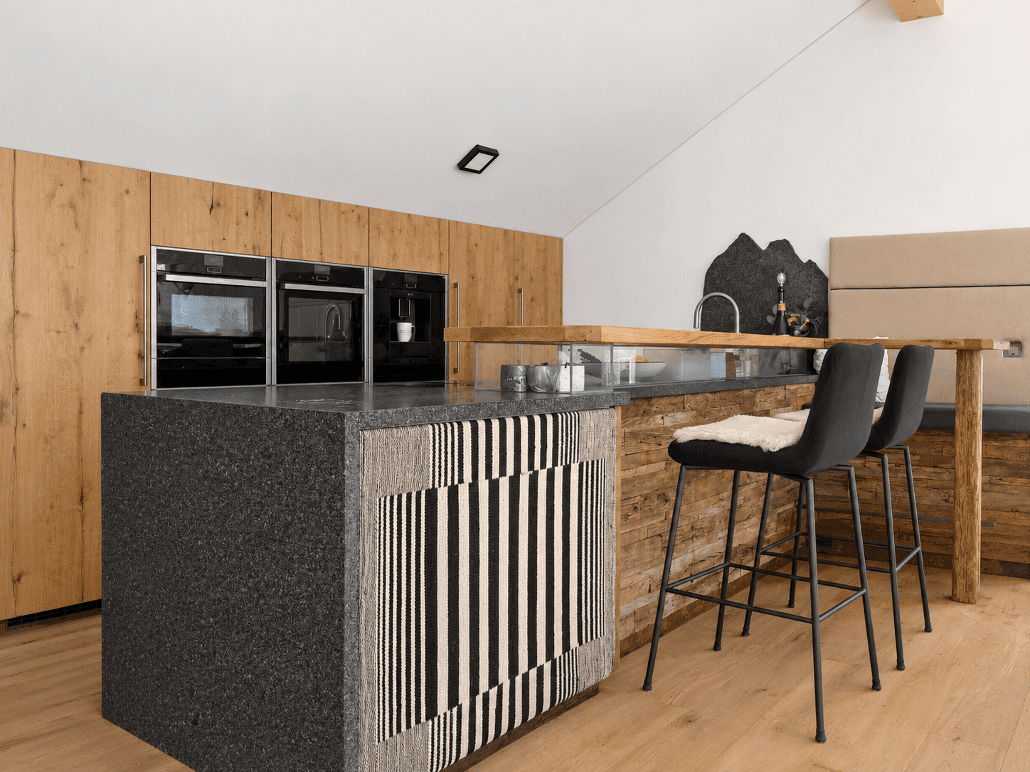 Moderne Küche mit Holzelementen, integrierten Geräten und einer stilvollen Kücheninsel mit Barhockern.