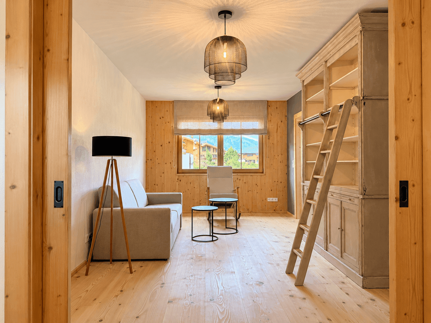 Gemütliches Zimmer mit Holzboden, Bücherregal und Blick auf die umliegende Berglandschaft.