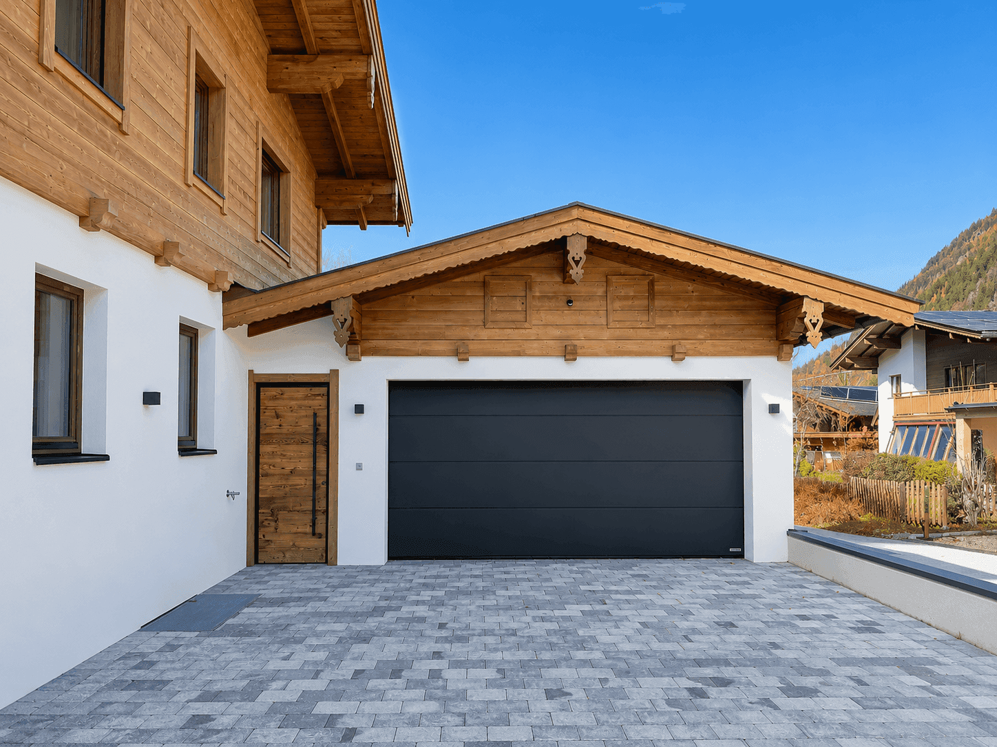 Integrierte Garage mit modernem, dunklem Tor und gepflasterter Zufahrt am Holzchalet.
