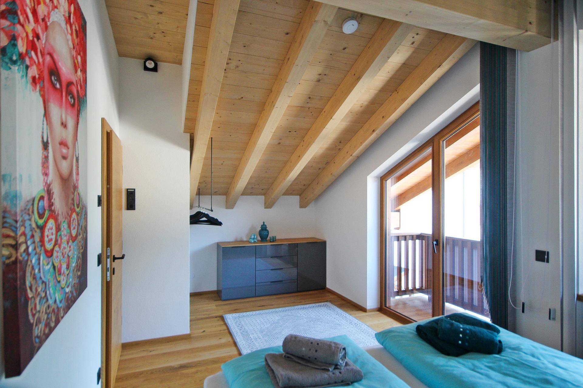 Schlafzimmer mit Holzbalkendecke, Holzboden und direktem Zugang zum Balkon.