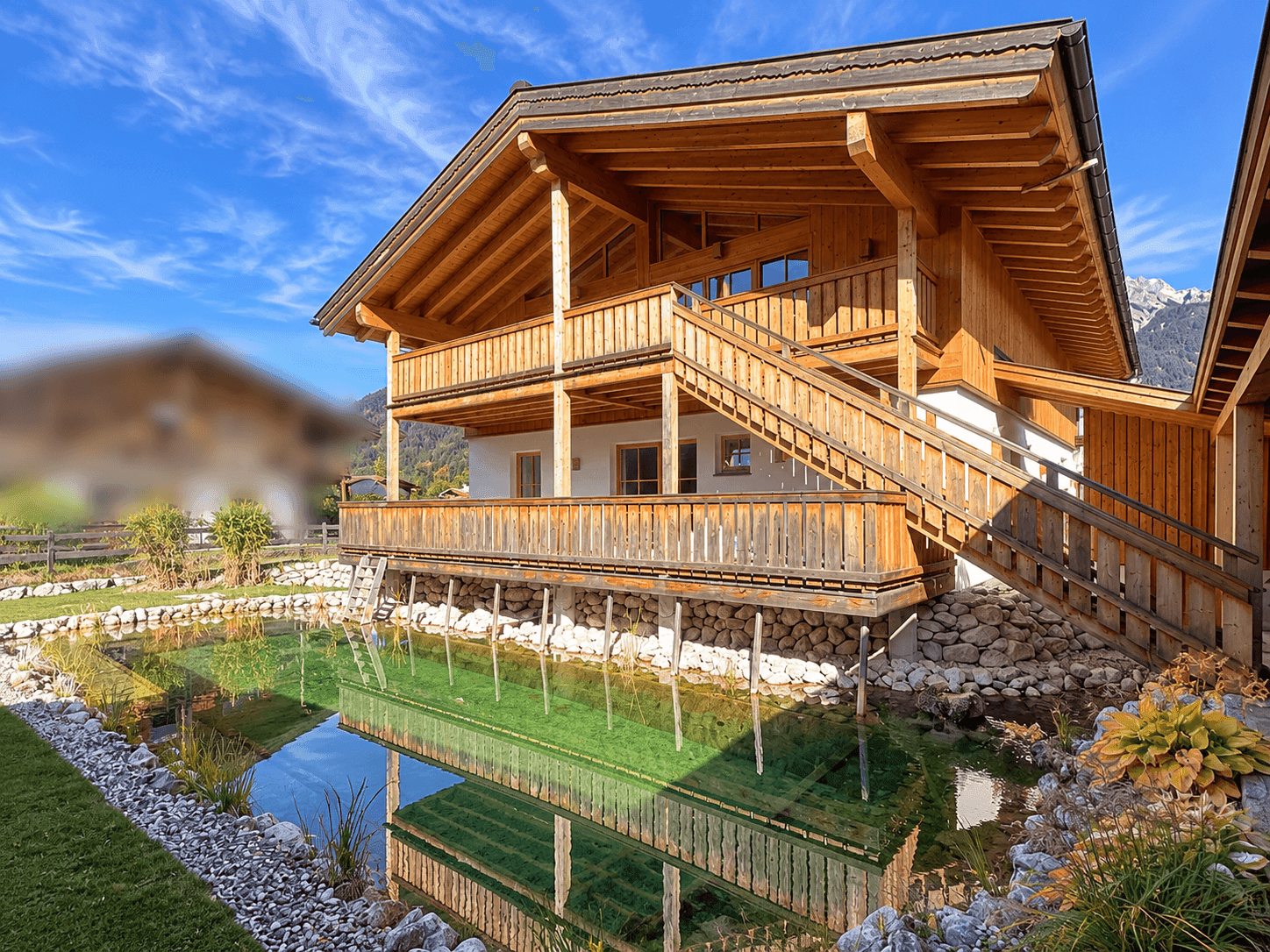 Charmantes Holzhaus mit Balkonen und einem idyllischen Teich im Vorgartenbereich.
