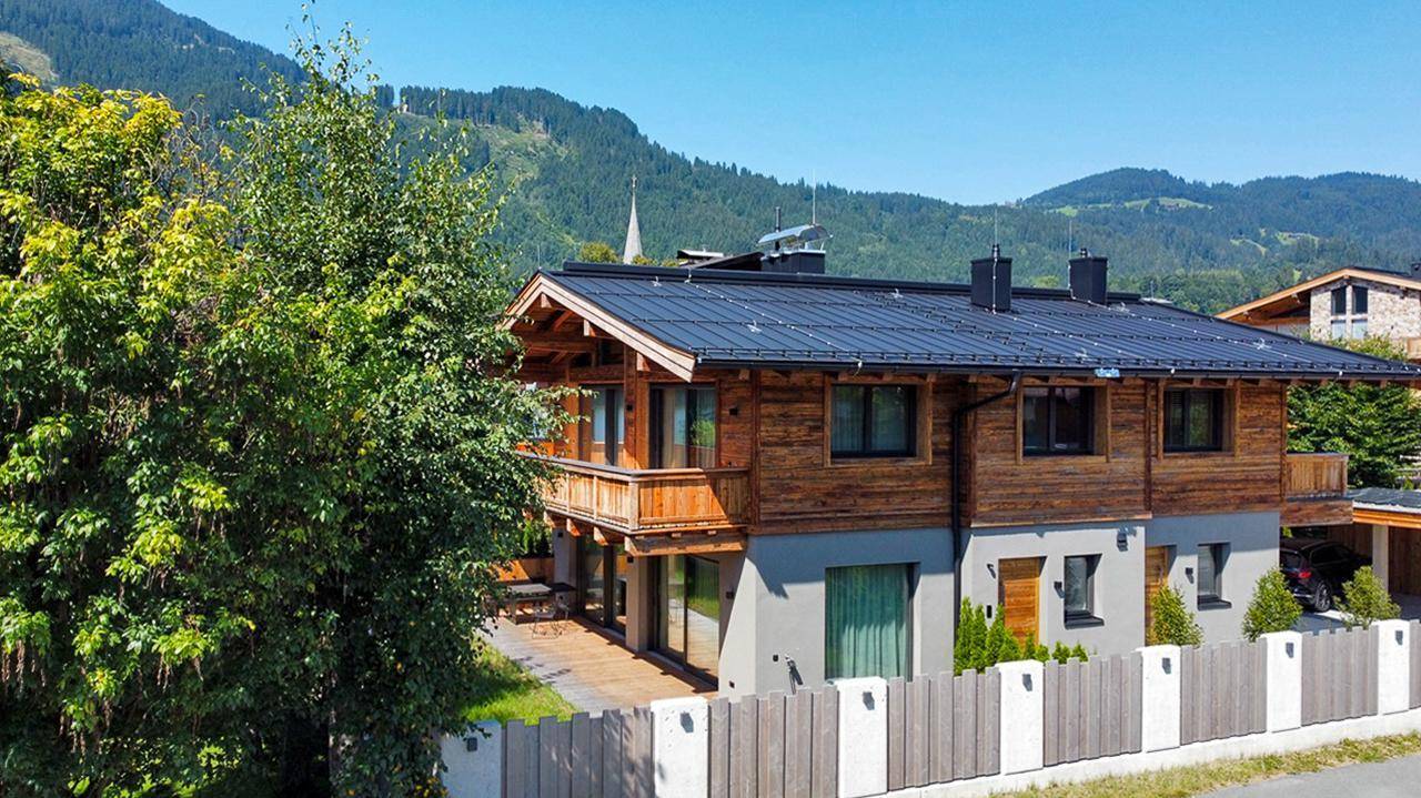 Modernes Chalet mit Holzfassade, Photovoltaikanlage und Bergblick in grüner Umgebung.