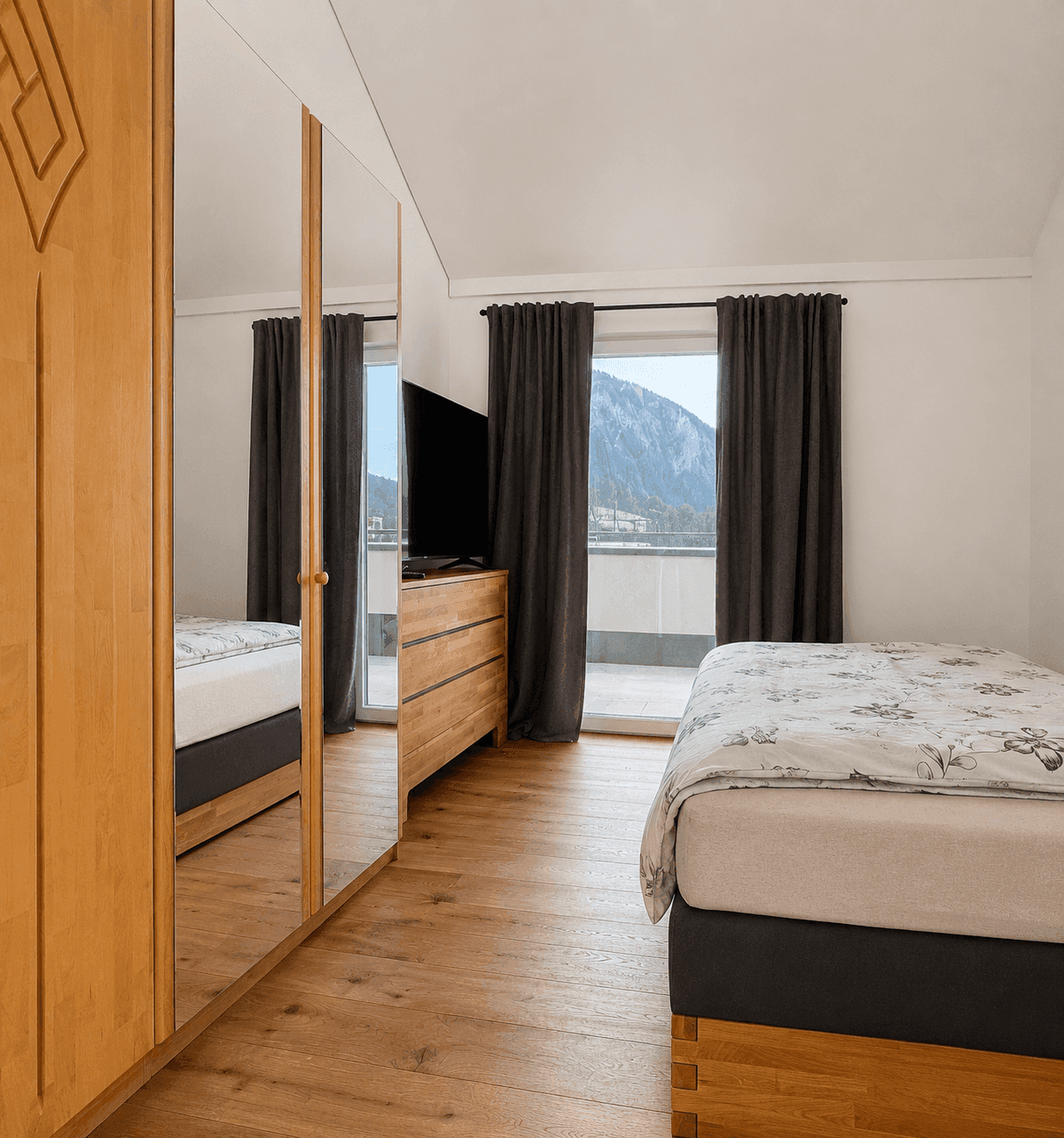Helles Schlafzimmer mit Holzboden, Spiegelschrank und Zugang zu einem Balkon mit Bergblick.
