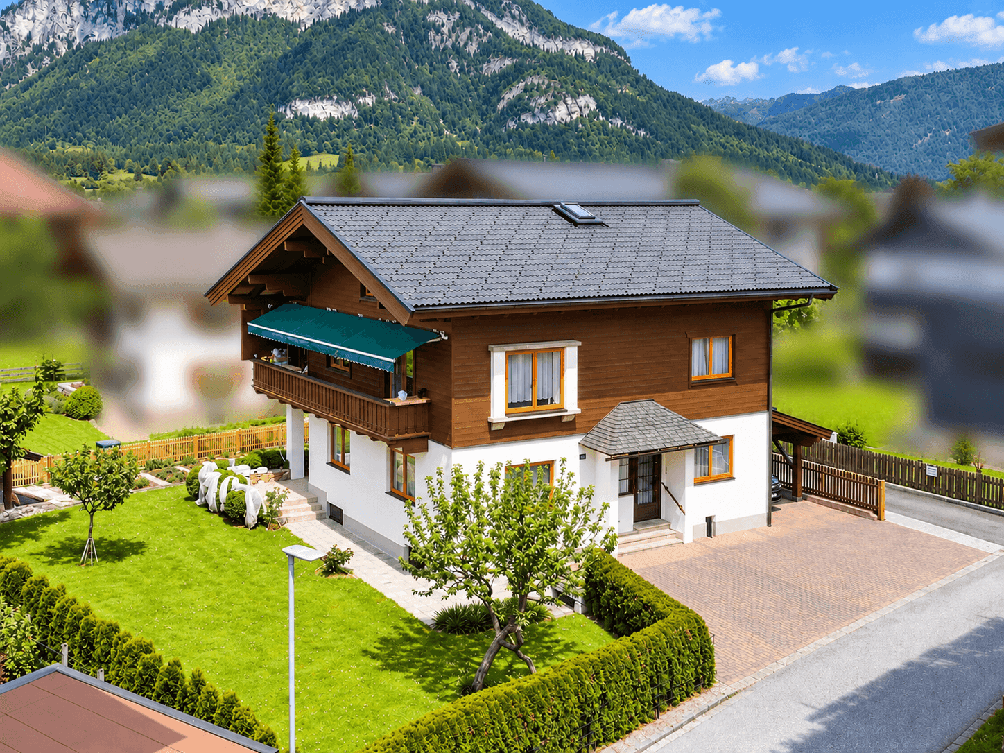 Panoramablick auf das Haus mit großem Garten, Einfahrt und beeindruckender Bergkulisse.