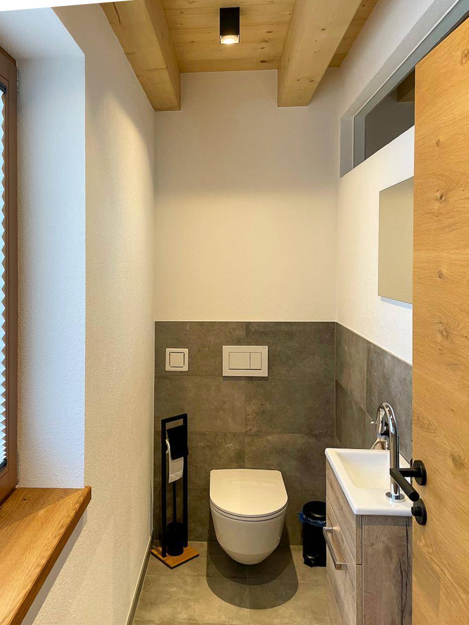 Praktisches Gäste-WC mit Wand-WC, kleinem Waschbecken und Fenster für Tageslicht.