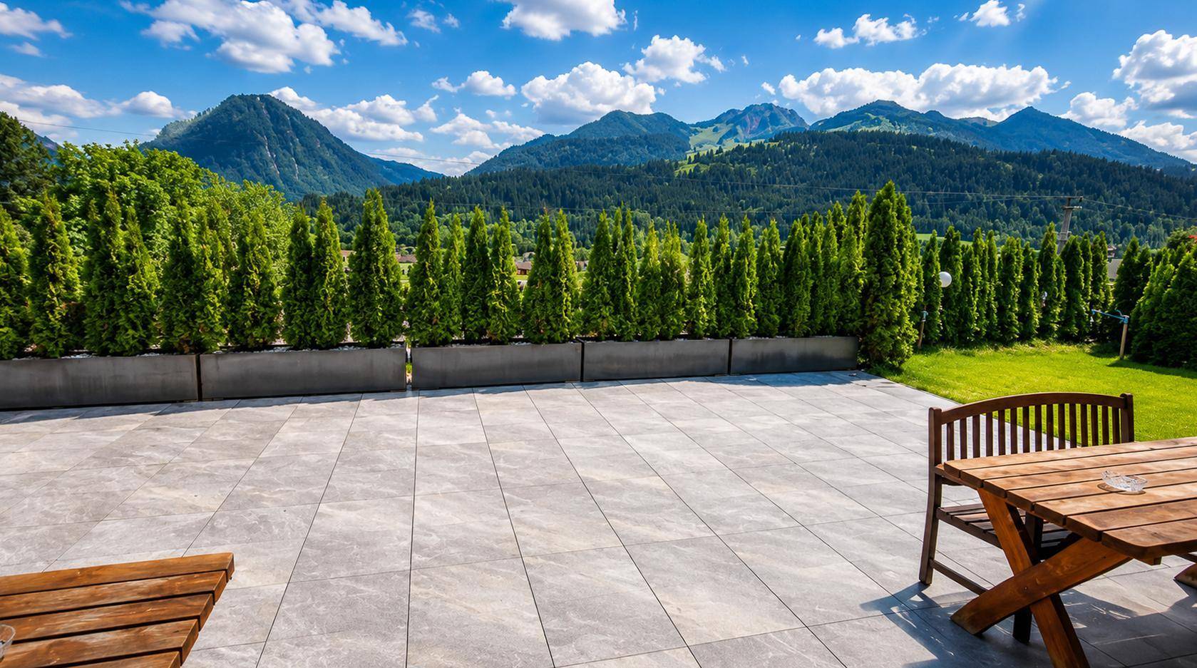Große, gepflasterte Terrasse mit Gartenmöbeln und Panoramablick auf die Berge.