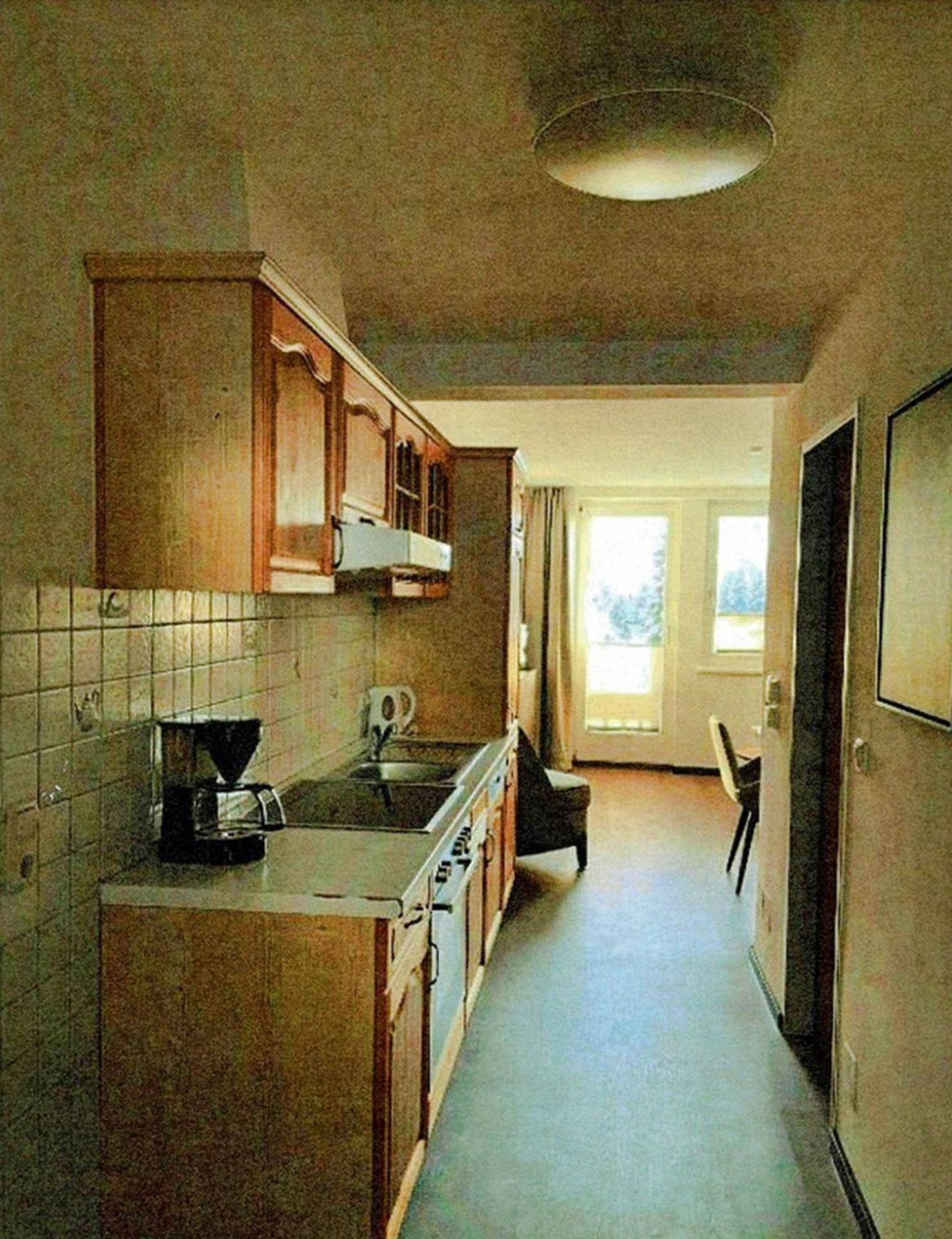 Kleine, funktionale Küche mit Holzschränken und Fliesenrückwand, angrenzend an einen Wohnbereich.