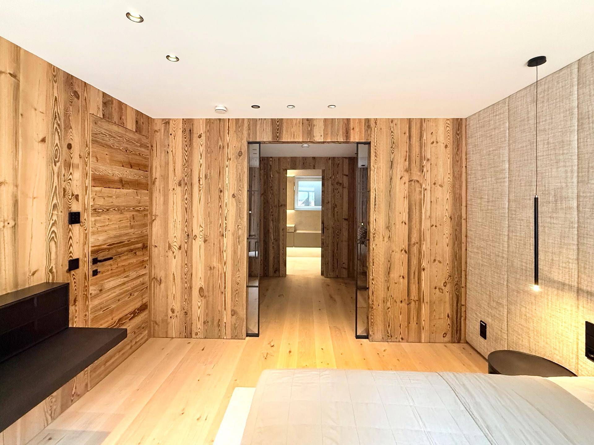 Schlafzimmer mit Holzwänden und Zugang zu einem weiteren Raum, bietet eine warme und natürliche Atmosphäre.