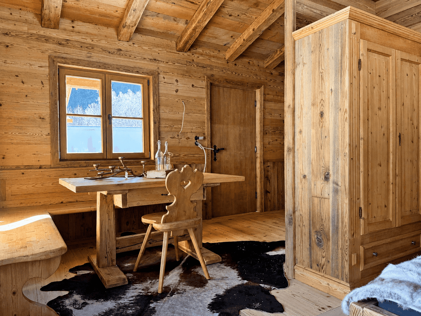 Rustikaler Essbereich mit Holztisch, Bänken und Kuhfellteppich in einem Holzhaus.