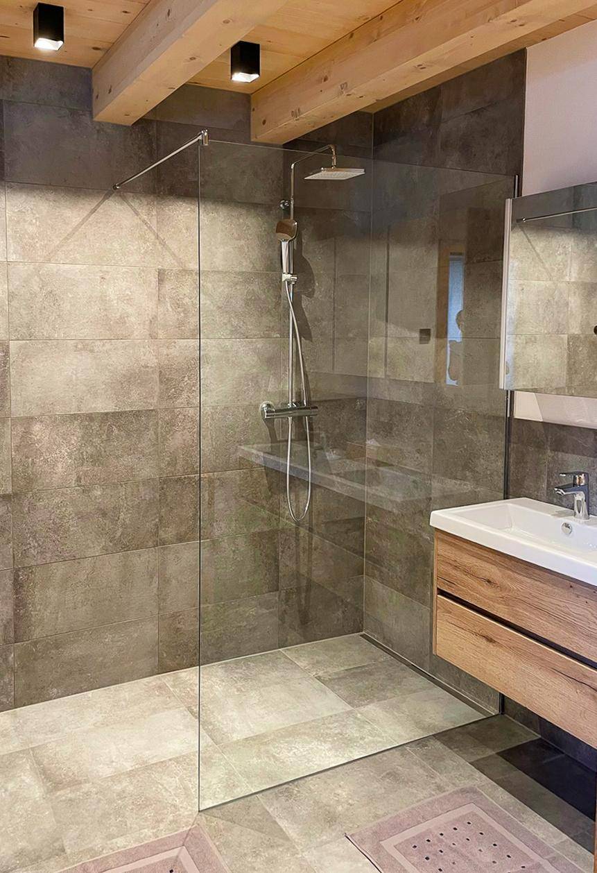 Helles Badezimmer mit begehbarer Dusche, modernen Armaturen und Holzbalkendecke.
