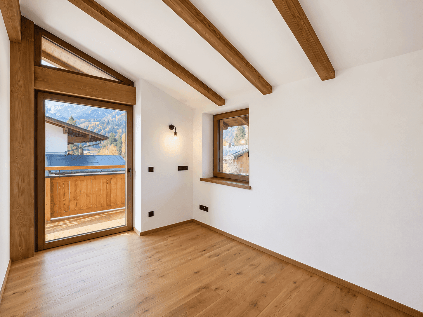 Helles Schlafzimmer mit Holzboden, sichtbaren Balken und Zugang zu einem Balkon mit Bergblick.