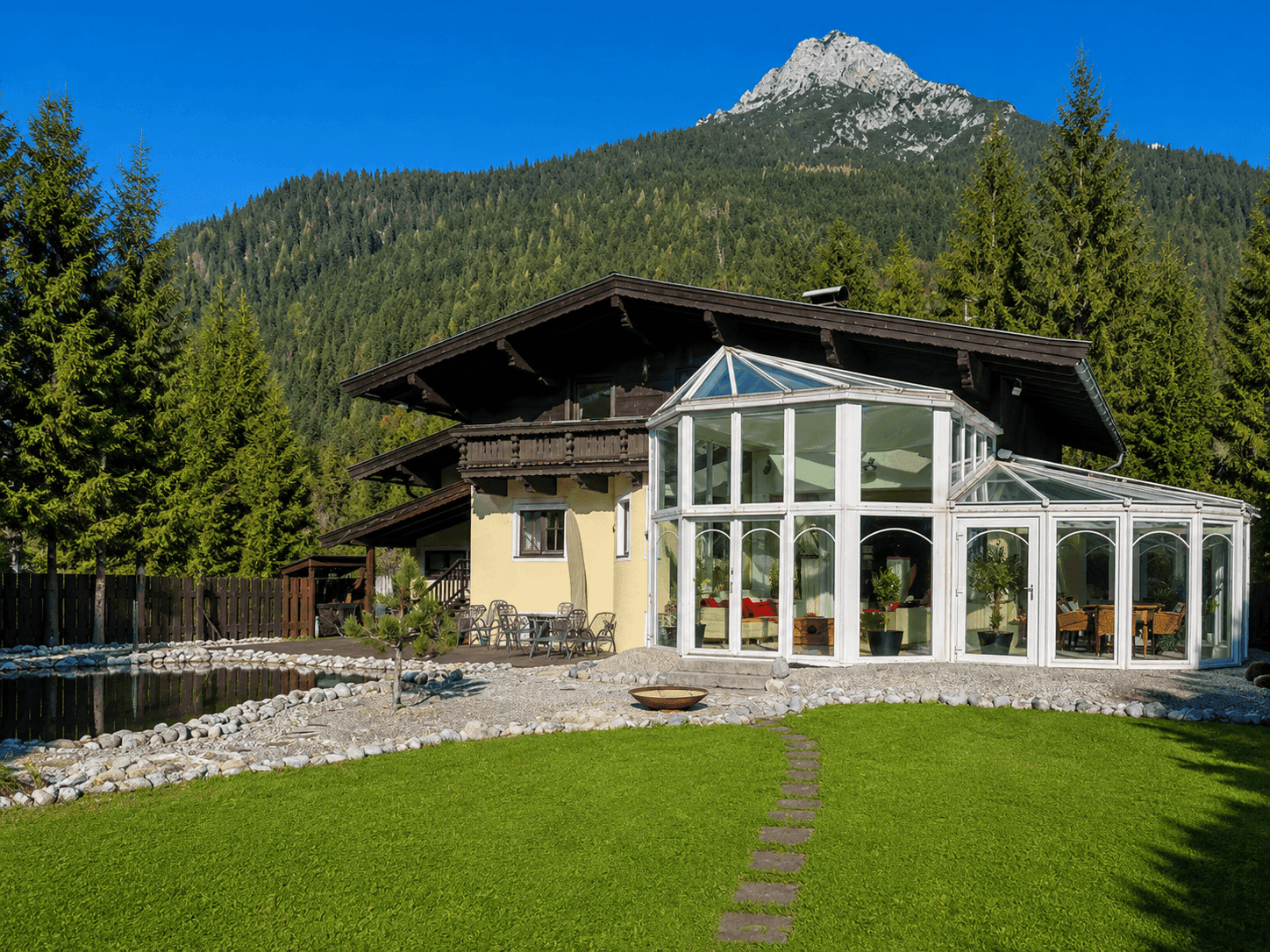 Malerisches Chalet mit Wintergarten und Bergblick, umgeben von grünen Bäumen und Natur.