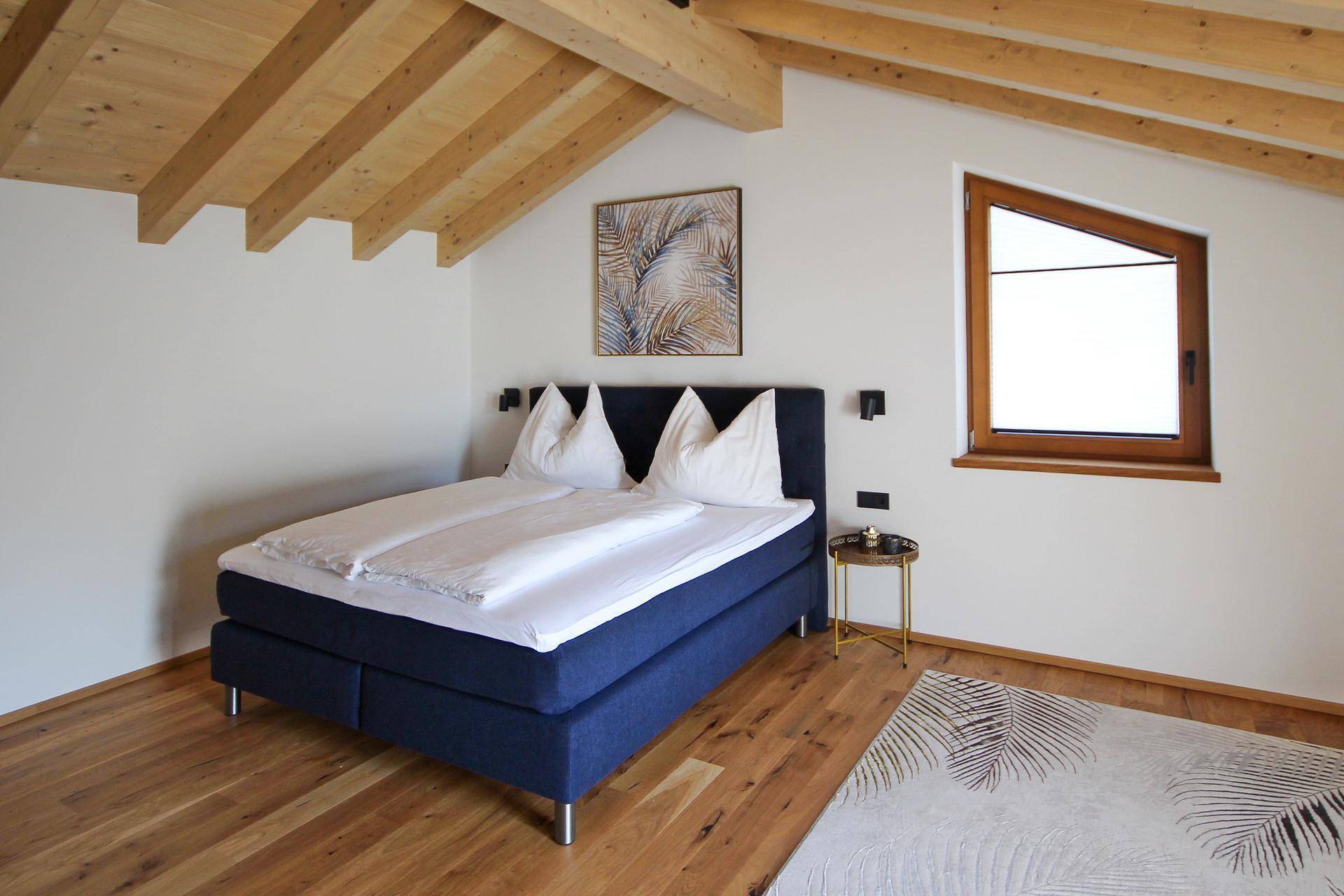 Geräumiges Schlafzimmer mit Holzbalkendecke, Holzboden und schrägem Fenster.
