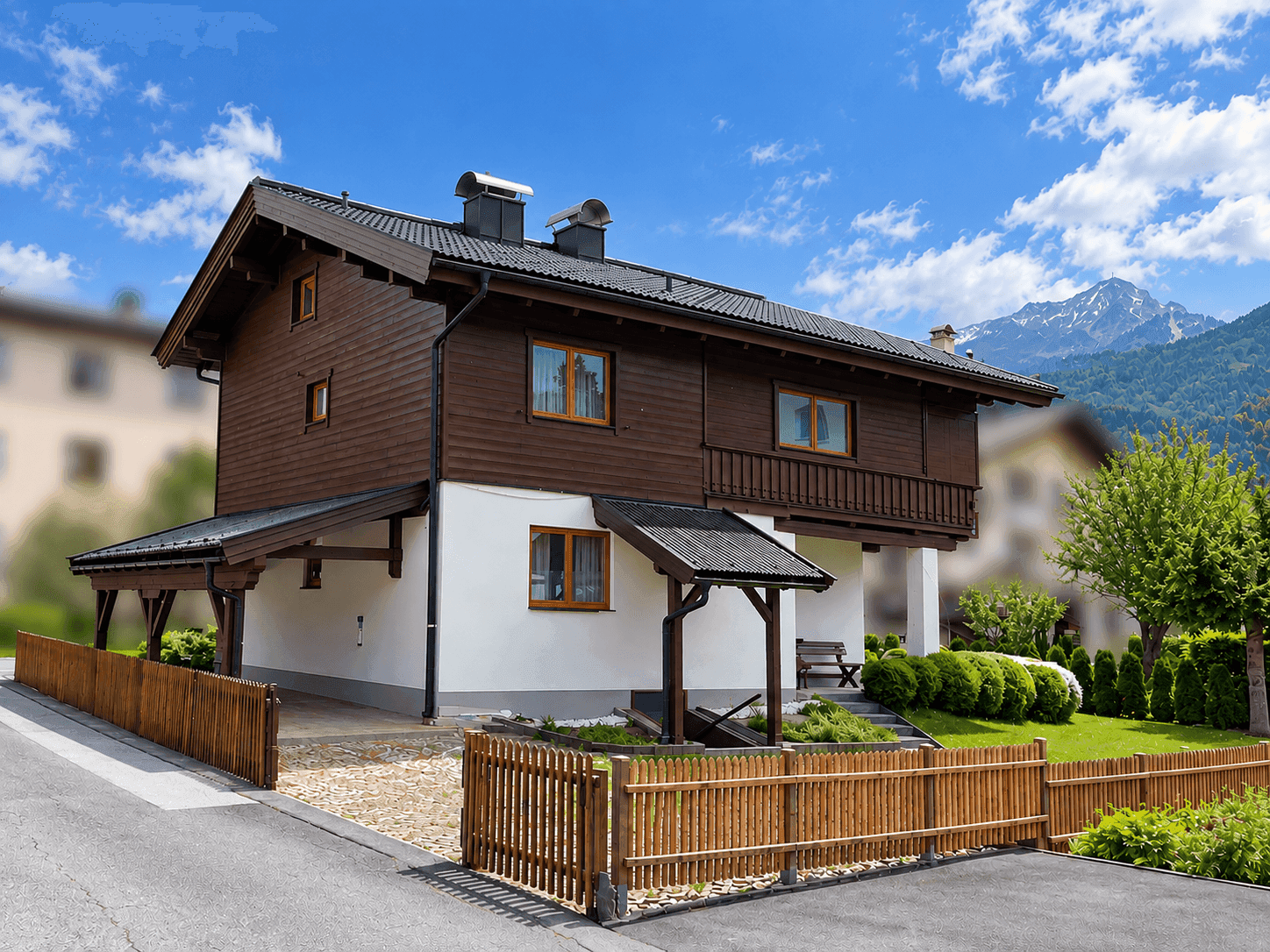 Seitenansicht des Hauses mit Carport, Holzzaun und malerischem Bergblick in der Ferne.