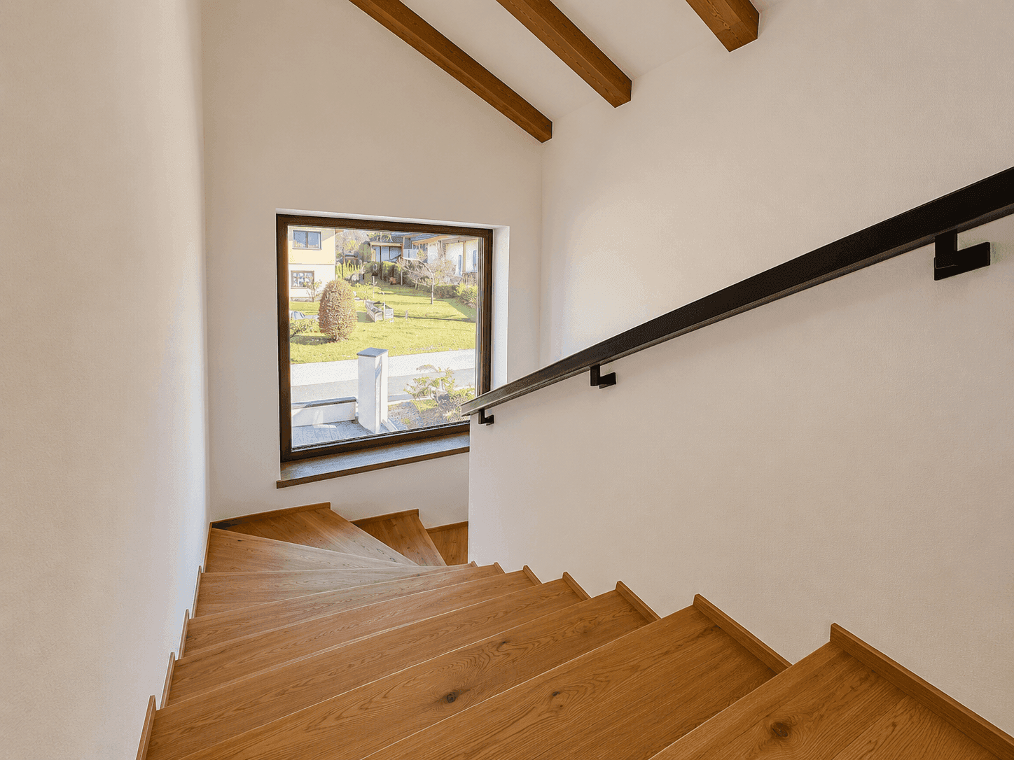 Holztreppe mit schwarzem Geländer und großem Fenster mit Blick auf den Garten.