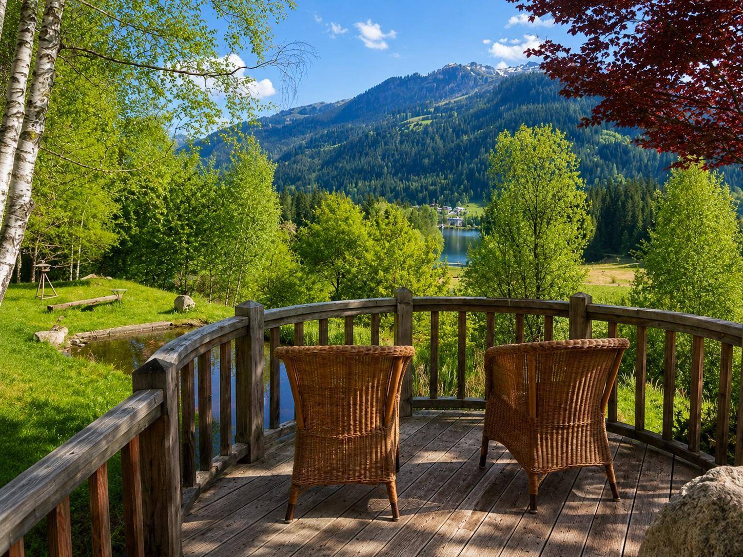 Gemütlicher Balkon mit Korbstühlen bietet einen malerischen Blick auf Berge, See und grüne Wälder.