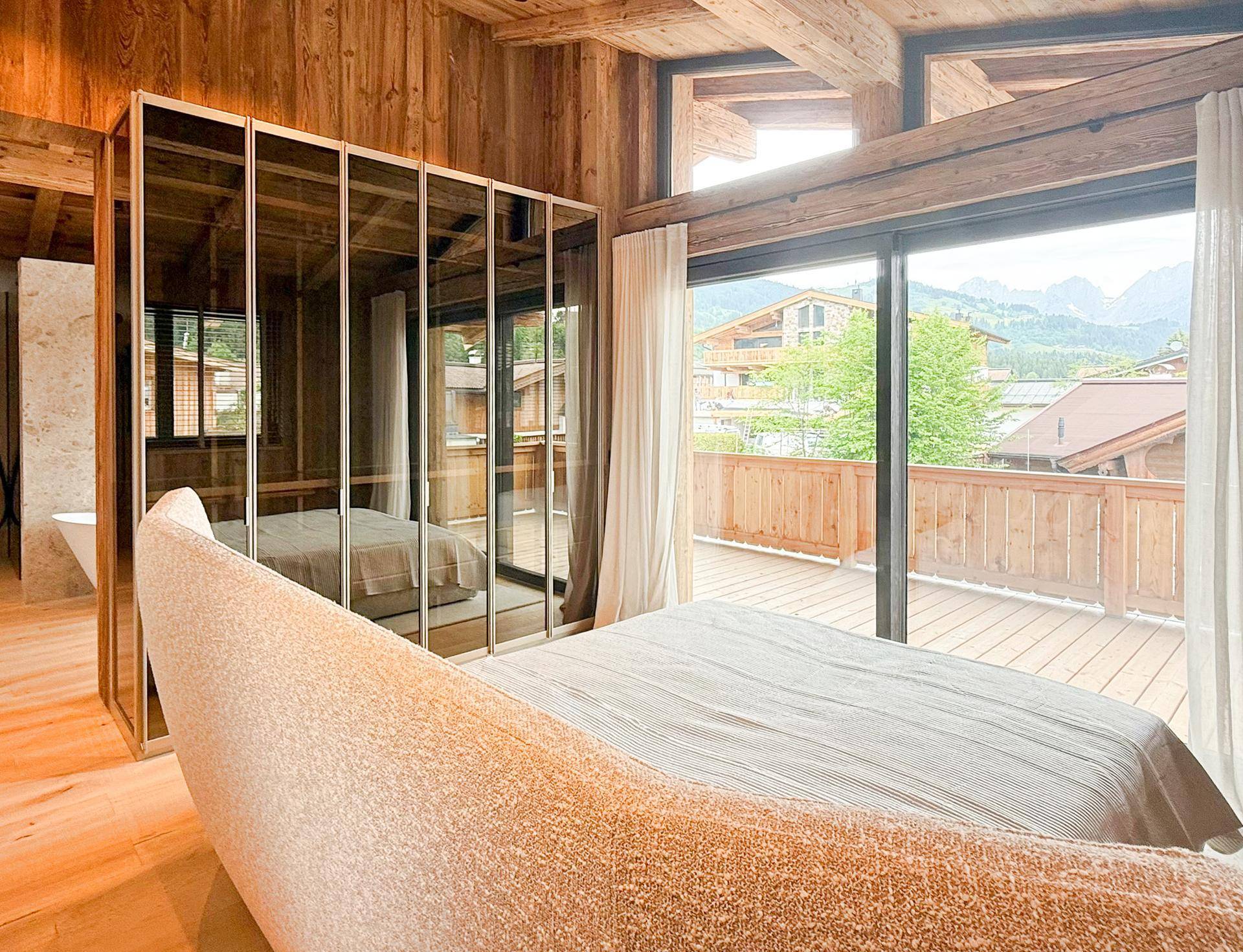 Schlafzimmer mit Holzbalkendecke, großen Fenstern und Zugang zur Terrasse mit Bergblick.