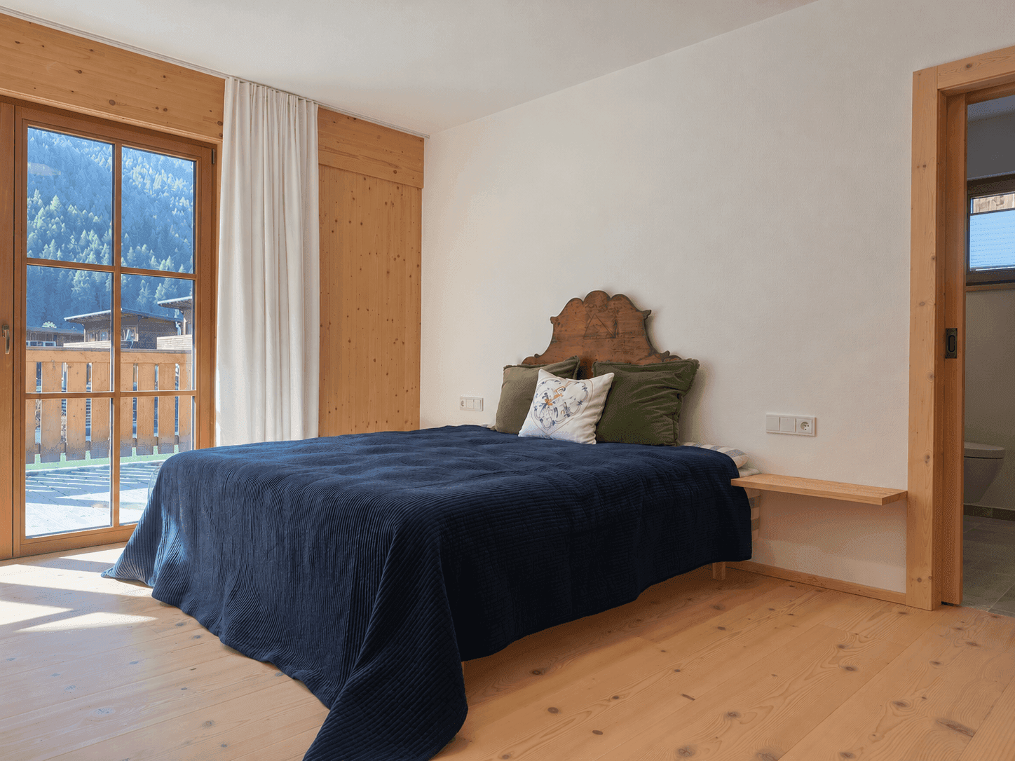 Helles Schlafzimmer mit Holzboden, traditionellem Bett und Zugang zum Balkon mit Bergblick.