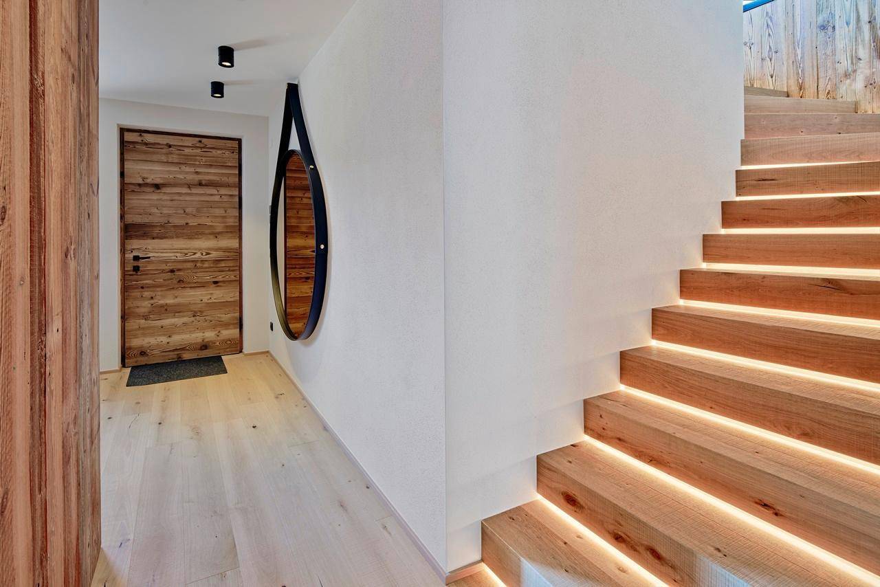 Heller Eingangsbereich mit Holztreppe, indirekter Beleuchtung und Holztür.