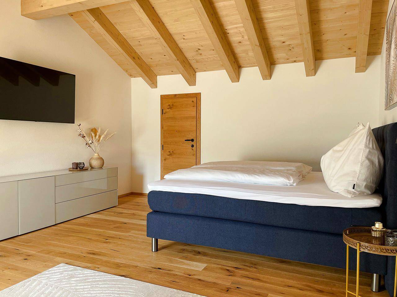 Helles Schlafzimmer mit Holzbalkendecke, Holzboden und moderner Einrichtung.