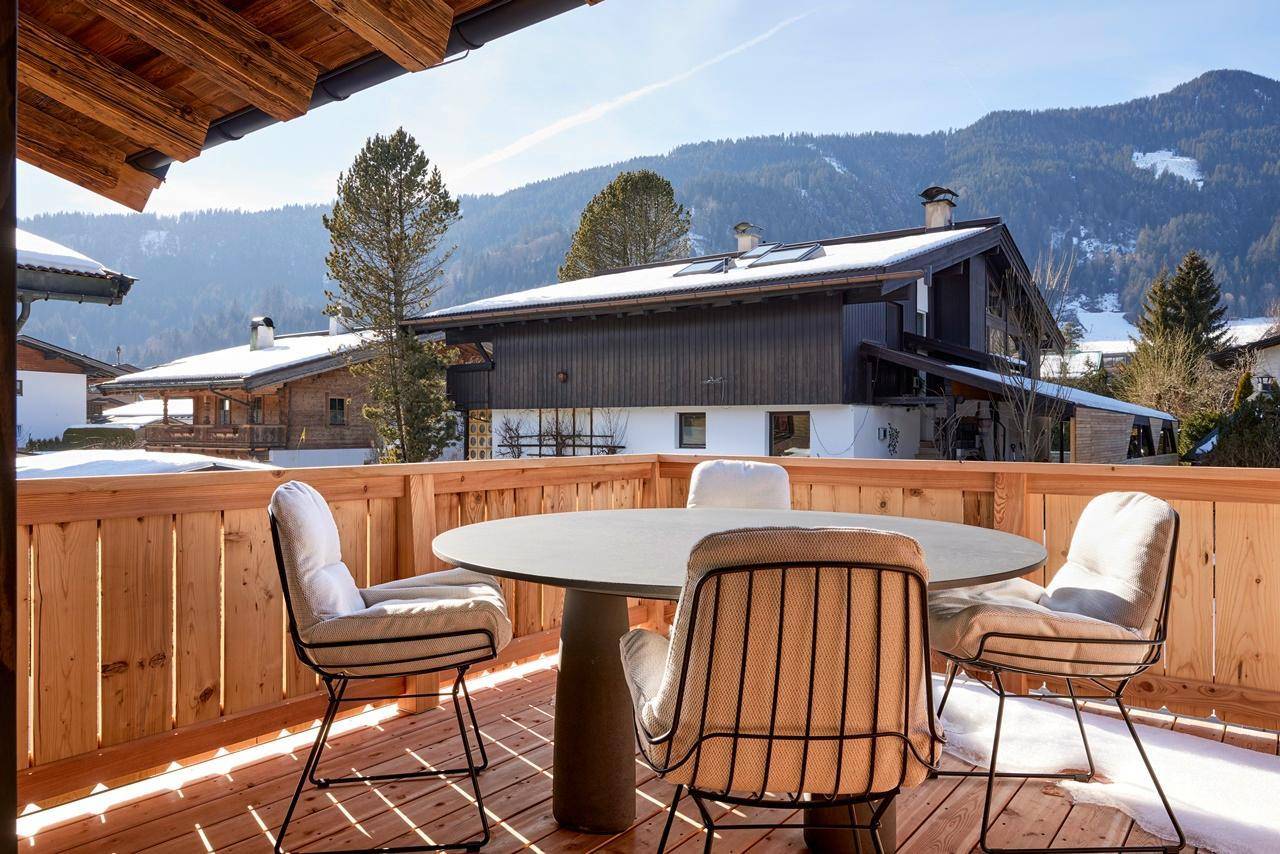 Sonniger Balkon mit Esstisch und Stühlen, umgeben von verschneiten Bergen, perfekt für Mahlzeiten im Freien.
