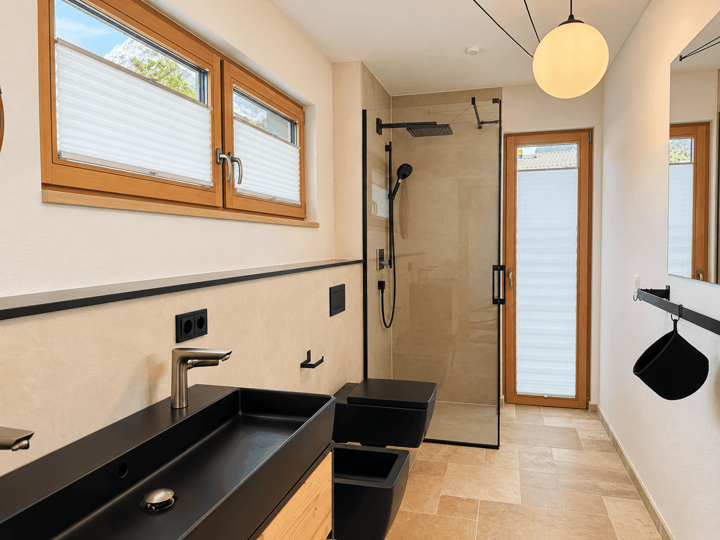 Modernes Badezimmer mit begehbarer Dusche, schwarzem Waschbecken und Fenster mit Bergblick.