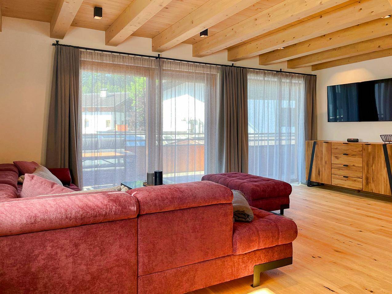 Gemütliches Wohnzimmer mit großem Sofa, Holzbalkendecke und Zugang zu einem Außenbereich.