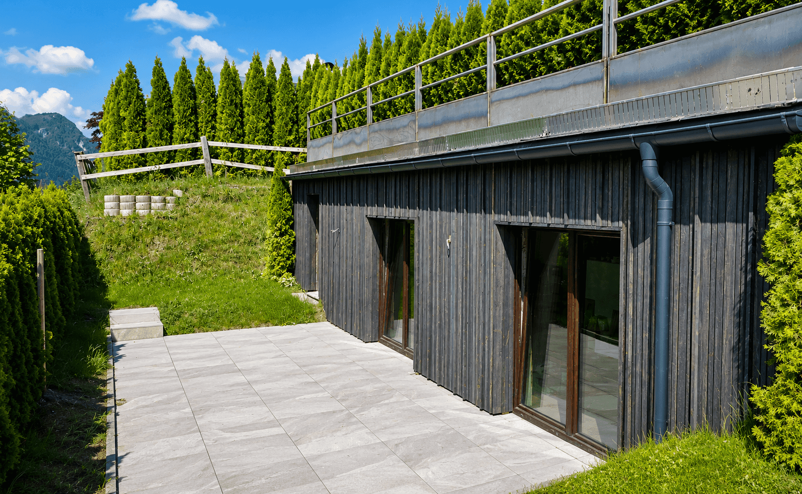 Moderne Gebäudefassade mit dunkler Holzverkleidung und angrenzender gepflasterter Terrasse.