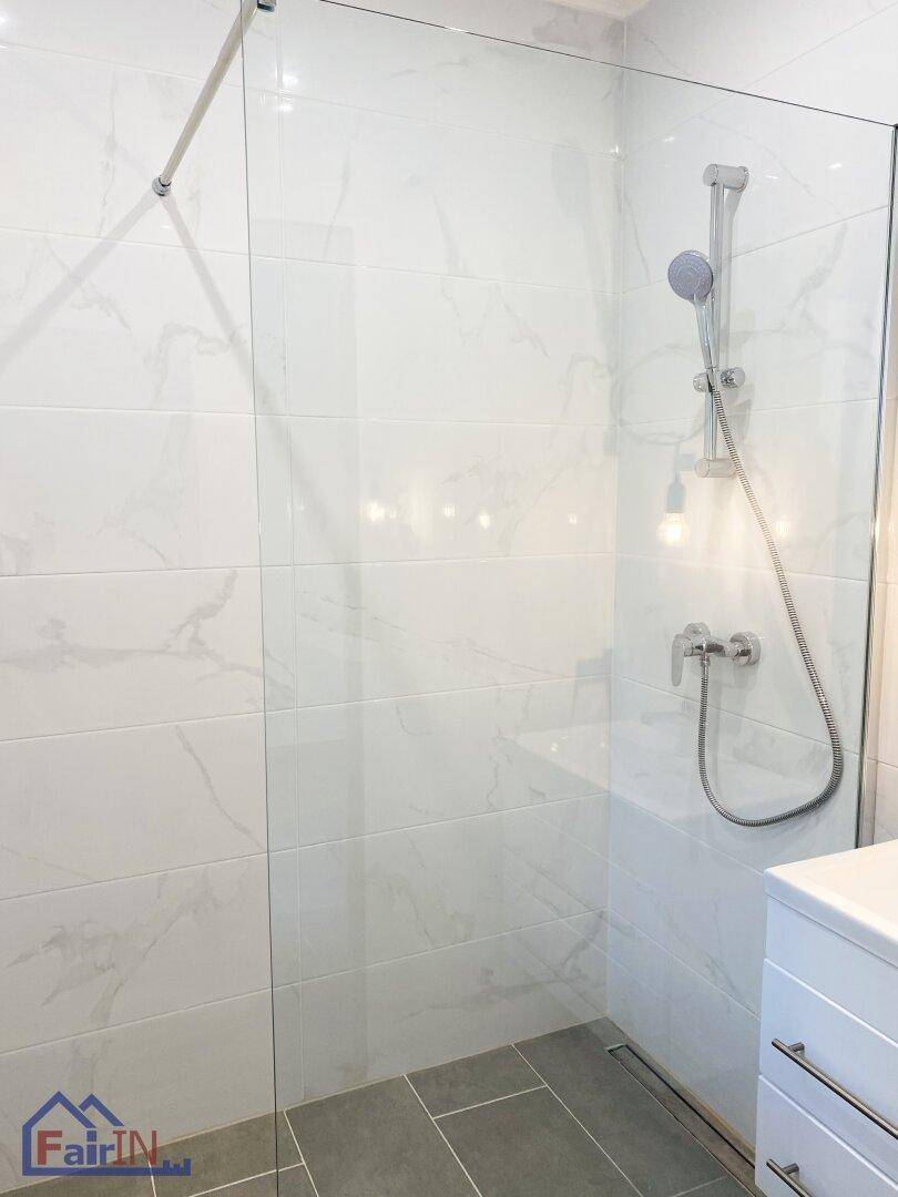 Moderne Duschkabine mit Glaswand und weißen Marmorfliesen in einem hellen Badezimmer.