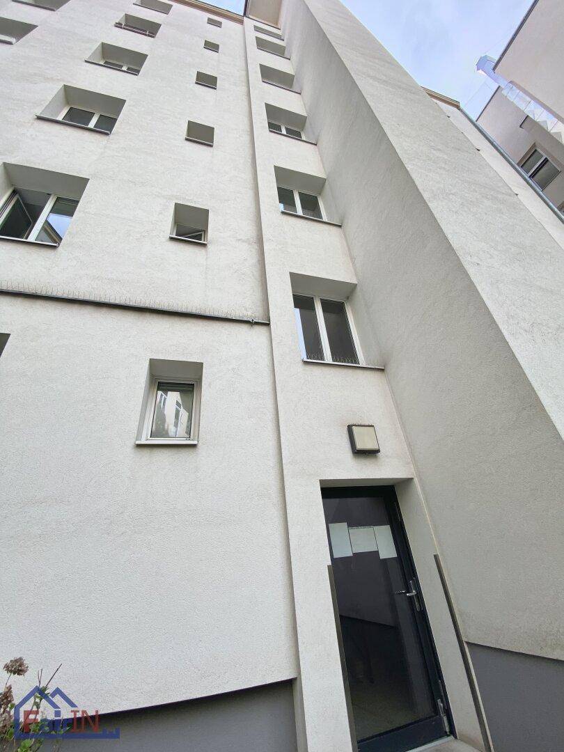 Hohe, weiße Fassade eines Mehrfamilienhauses mit zahlreichen Fenstern und Eingangstür.